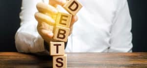 Person stacking blocks with letters D-E-B-T-S written on them to spell out DEBTS