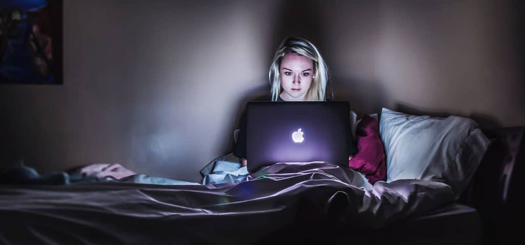 Woman sitting in bed in the dark using laptop computer