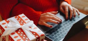 Woman using keyboard on laptop with a holiday gift sitting next to her