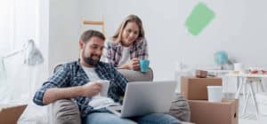 Couple relaxing during home renovation looking at laptop screen holding cups of coffee