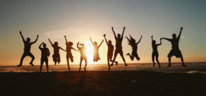 Group of people jumping in air with hands and feet outright on top of mountain in front of sunset