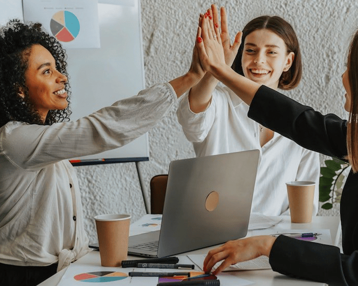 Three diverse woman sitting around table for meeting high-fiving